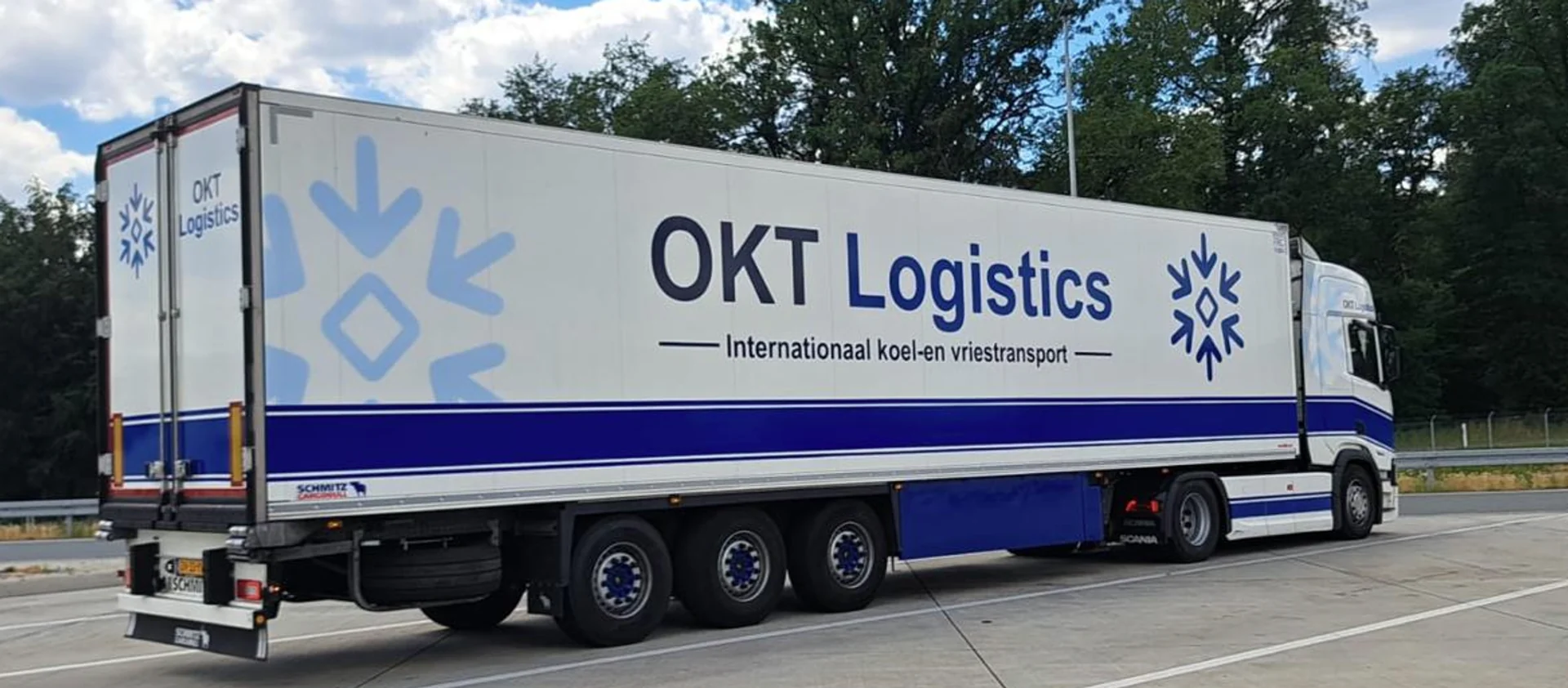 Side and rear view of an OKT Logistics truck with an enclosed refrigerated trailer in a parking area